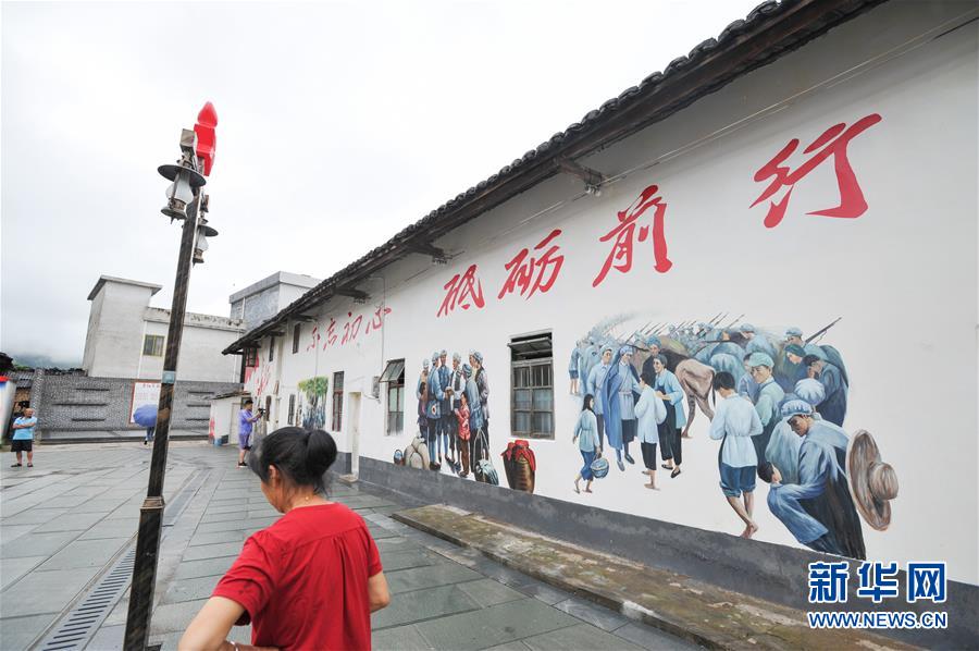 6月23日,在广东省南雄市油山镇上朔村,一名村民从画有长征题材壁画