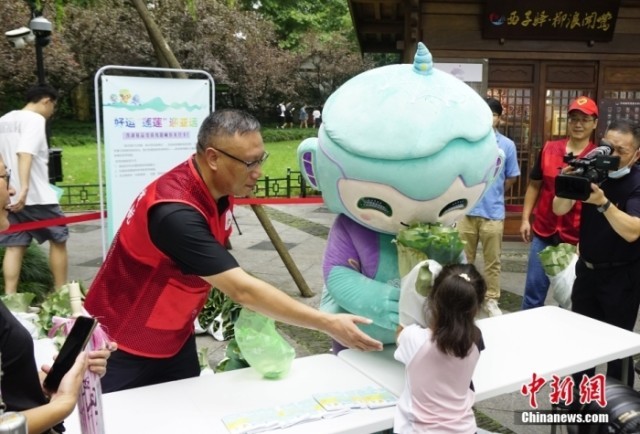 杭州亚运会吉祥物“琮琮”“宸宸”“莲莲”在浙江杭州西湖畔参加莲蓬荷叶义卖活动，图为亚运会吉祥物“莲莲”将分包好的莲蓬、荷叶交给顾客。<a target='_blank' href='/'><p  align=